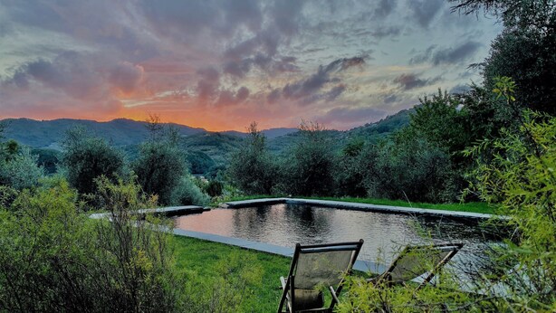 Un área de piscina tranquila al aire libre con una silla, rodeada de exuberante vegetación y colinas al fondo.