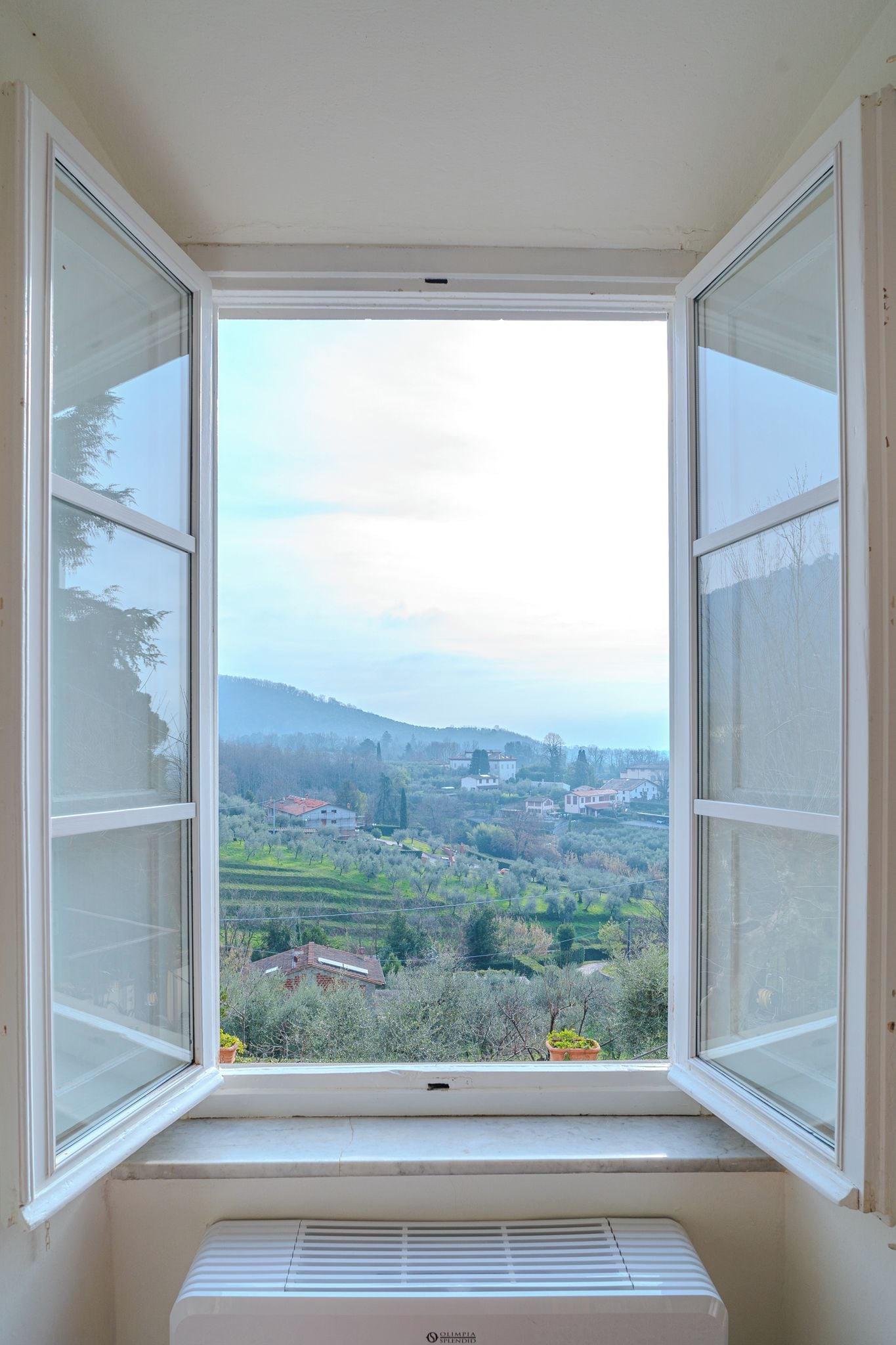 A window with a view of a rural landscape, including houses and trees.