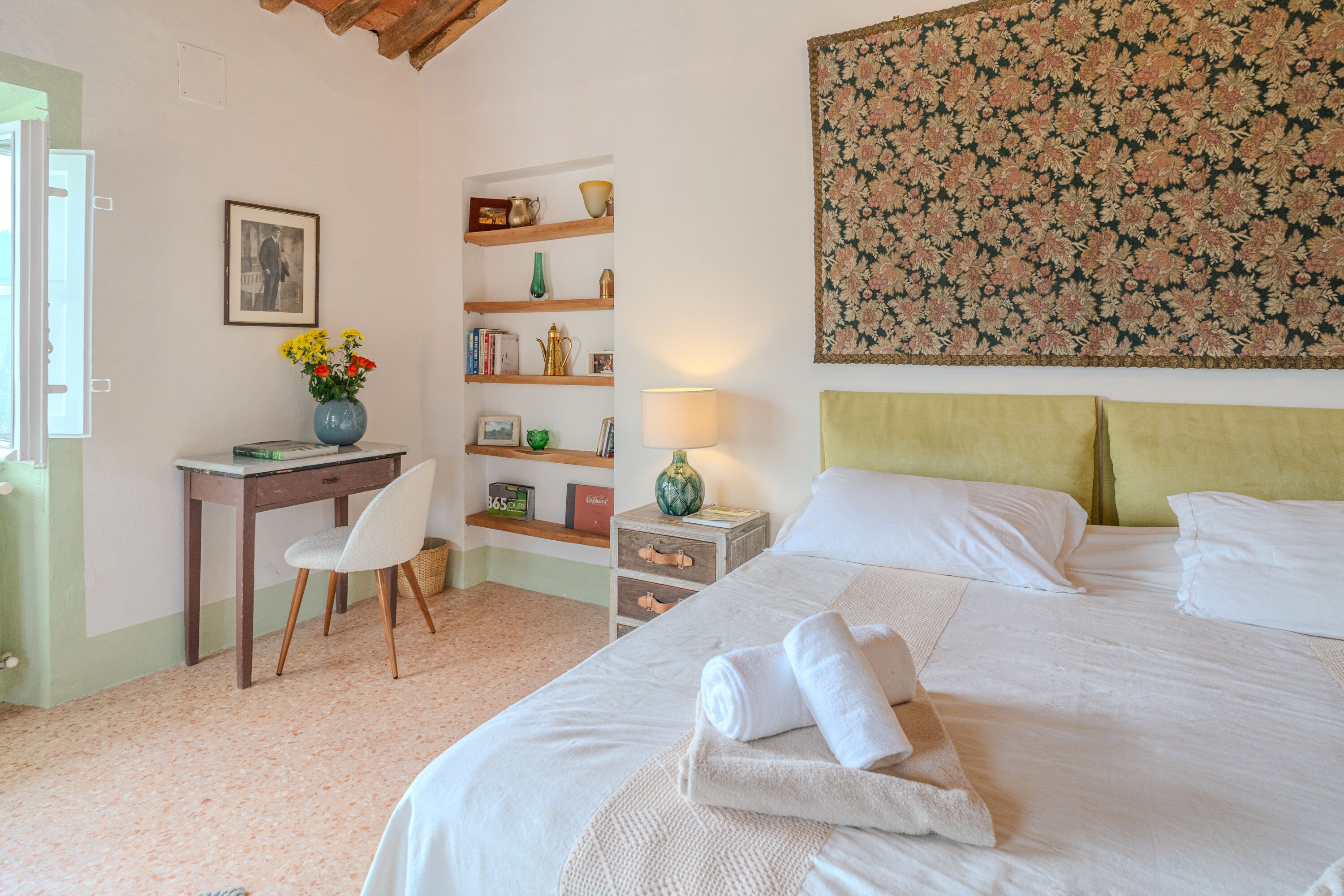 Un dormitorio con cama, escritorio, silla, mesita de noche y lámpara de pared.