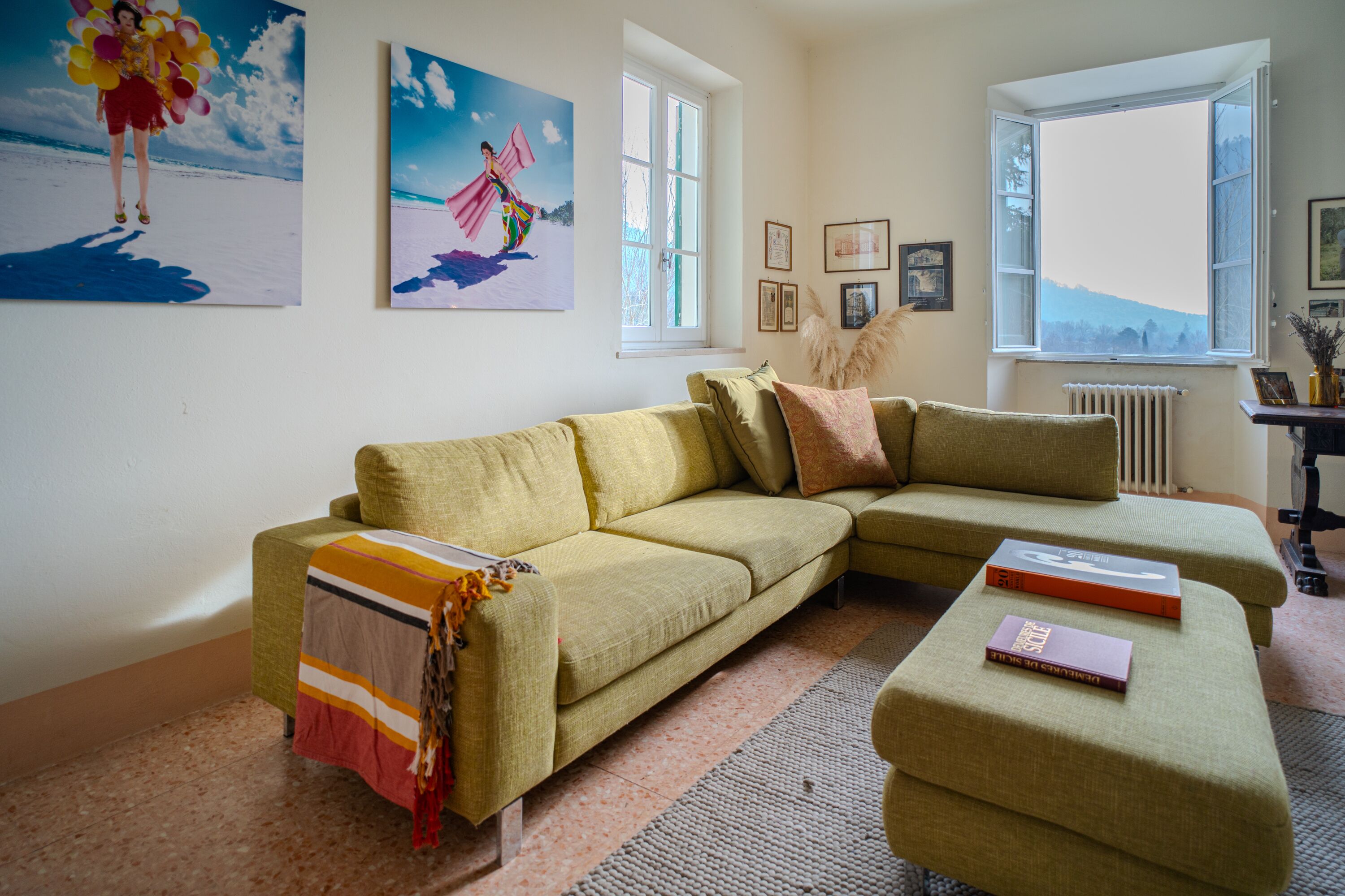 Ein Wohnzimmer mit einem grünen Sofa, einem passenden Hocker und einem Fenster mit Blick ins Freie.