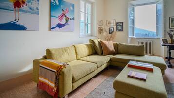Ein Wohnzimmer mit einem grünen Sofa, einem passenden Hocker und einem Fenster mit Blick ins Freie.
