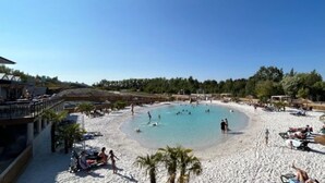 Ranta, jossa on uima-allas, palmuja sekä ihmisiä uimassa ja auringonotossa.