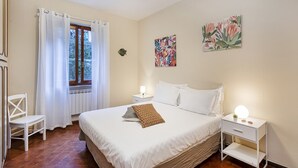 A neatly arranged bedroom with a bed, a bedside table with a lamp, a chair, and a window with curtains. - Una Palma a Camogli by Wonderful Italy (Camogli)