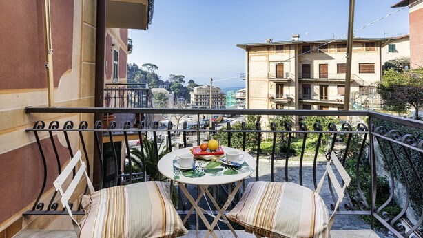 A balcony with two striped cushioned chairs and a small round table with a fruit bowl, a cup, and a book. - Una Palma a Camogli by Wonderful Italy (Camogli)