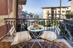 Ein Balkon mit zwei gestreiften Sitzgelegenheiten, einem kleinen runden Tisch mit Obstschale, Tasse und Buch.
