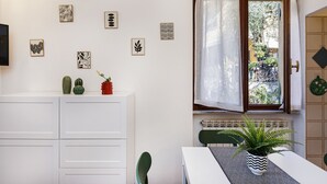 A room with a white cabinet, a dining table with a patterned table runner, and a window with a sheer curtain. - Una Palma a Camogli by Wonderful Italy (Camogli)