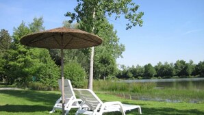 A grassy area with two white lounge chairs and a thatched umbrella.