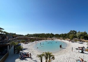 A beach resort with a large pool, sun loungers, and a sandy beach area.