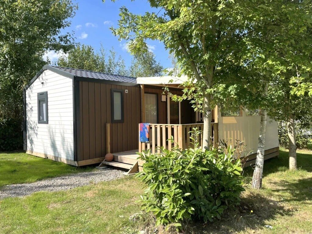 A small cabin with a wooden deck and a covered porch, surrounded by greenery.