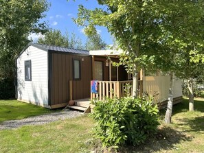 Eine kleine Holzhütte mit einer Holzterrasse und einer überdachten Veranda, umgeben von Grün.