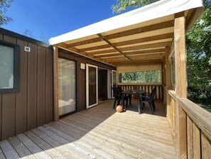 Eine Holzterrasse mit überdachter Veranda, einer Schiebetür und einem Tisch mit Stühlen.