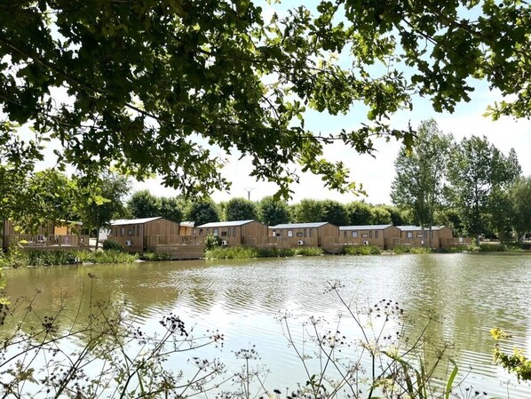 A row of wooden cabins by a calm lake, surrounded by lush greenery.