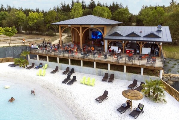 A beachside resort with a covered bar area, lounge chairs, and a pool.