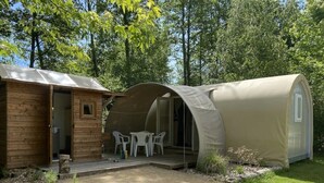 Maalaishenkinen mökki, jossa on puinen ulkoverhous ja suuri, beige telttaa muistuttava rakenne.