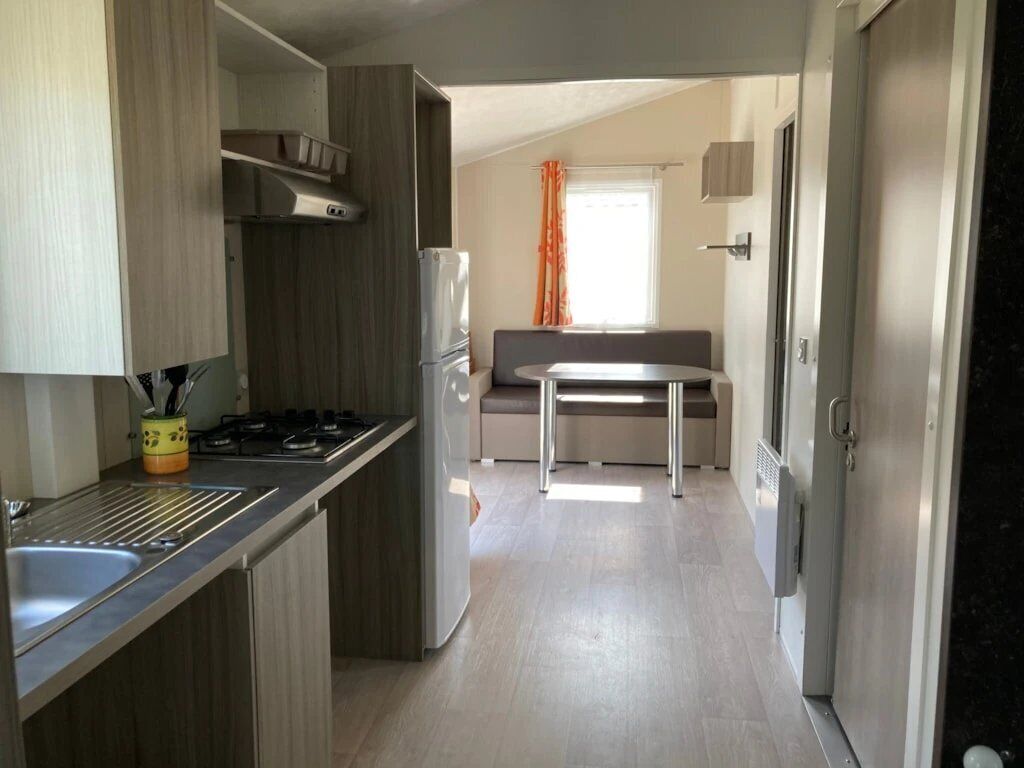 Cocina compacta con estufa a gas, lavamanos y refrigerador. Hay un comedor con mesa y sillas.