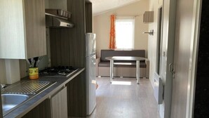 A compact kitchen with a gas stove, sink, and a refrigerator. There is a dining area with a table and chairs. - ZEcamping 4 étoiles espace aquatique locatif 31m2 (Aubigny-Les Clouzeaux)