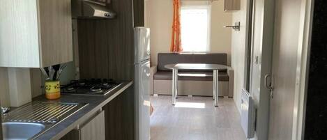 Cocina compacta con estufa a gas, lavamanos y refrigerador. Hay un comedor con mesa y sillas.