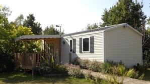 A single-story mobile home with a covered porch, a small garden, and a wooden deck. - ZEcamping 4 étoiles espace aquatique locatif 31m2 (Aubigny-Les Clouzeaux)