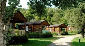 Een rij houten hutten met een gazen pad er naartoe, omgeven door bomen.