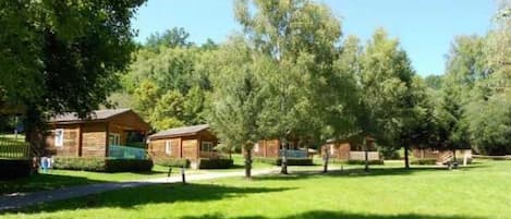 Une rangée de chalets en rondins, avec une pelouse verdoyante et des arbres en arrière-plan.