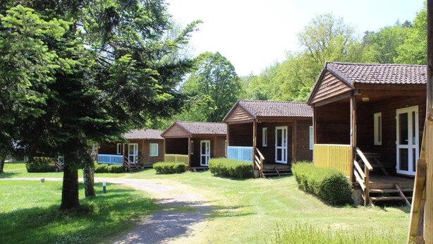 A row of wooden cabins with porches, surrounded by greenery and trees.