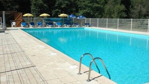 A swimming pool with a tiled deck, lounge chairs, and umbrellas.
