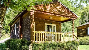 A wooden cabin with a porch, surrounded by trees and greenery.