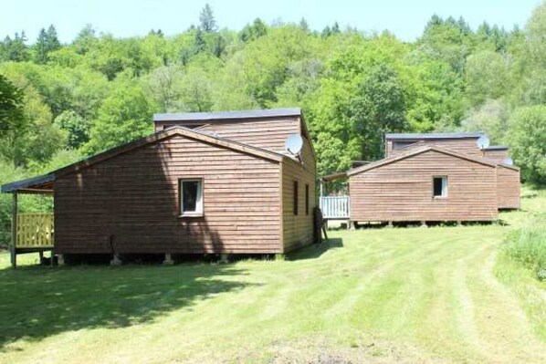 Two wooden cabins with pitched roofs, surrounded by a grassy area and dense forest.