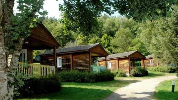 Une rangée de cabanes en bois, reliées par un sentier bordé d’herbe, et entourées d’arbres.