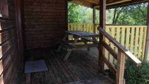 Une cabane en bois dotée d’un porche couvert, d’une table de pique-nique et d’un banc.