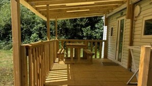 A wooden deck leading to a house with a covered porch and a small table.