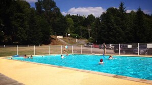 A swimming pool with people playing, surrounded by a fence and trees.