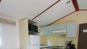Cocina compacta con refrigerador, microondas, estufa y alacenas. Hay un cesto de basura y un sofá en la sala.