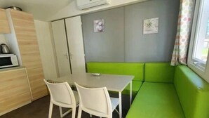 Une cuisine de taille réduite, avec une table et des chaises, un banc vert rembourré et une fenêtre avec un rideau.