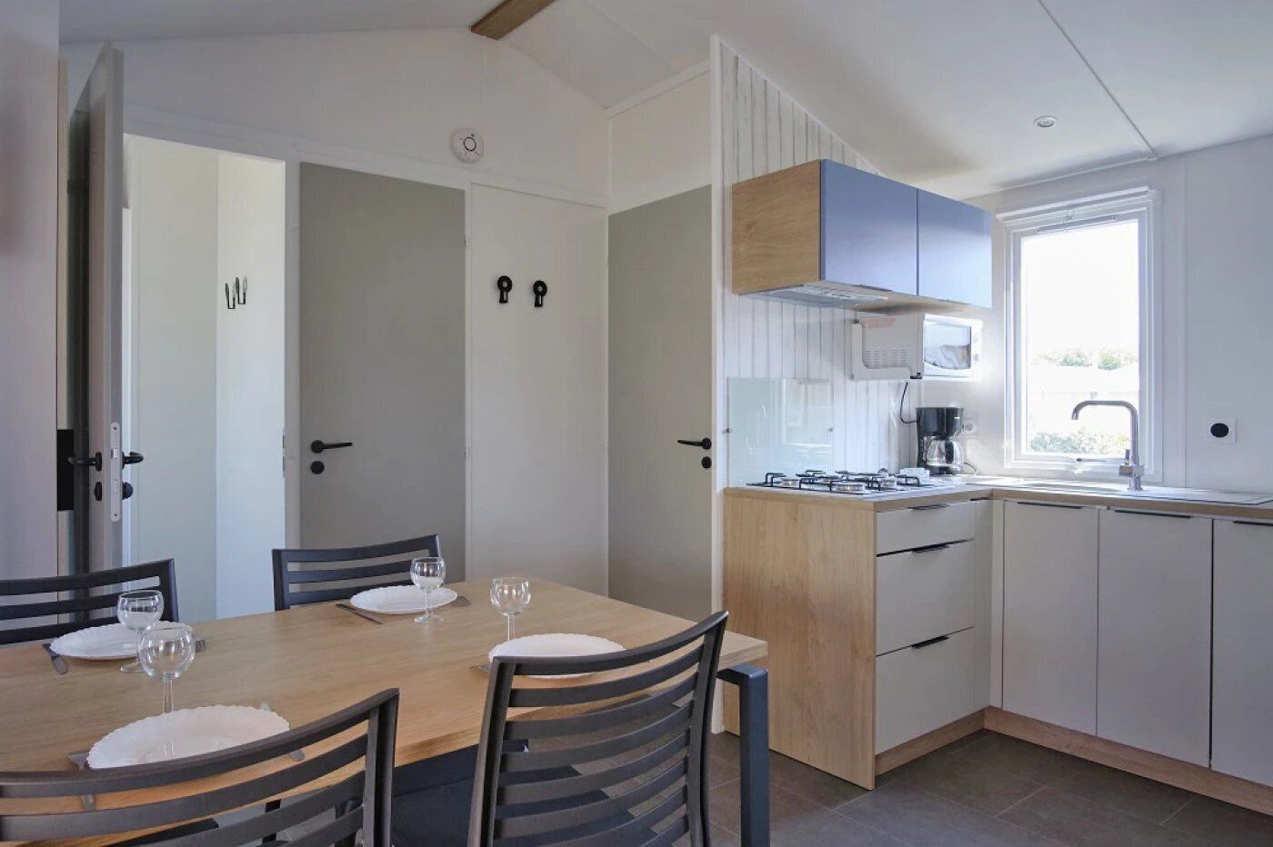 A modern kitchen with a dining area. It includes a wooden table with chairs, a gas stove, a sink, and cabinets.