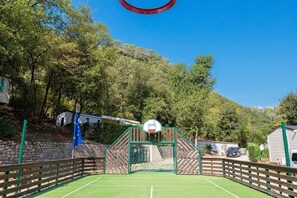 Ein Basketballplatz im Freien mit Holzzaun, Bäumen und blauem Himmel.
