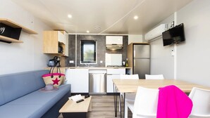 A compact kitchenette with a stove, sink, and refrigerator. There is a blue sofa and a wooden table with chairs. - ZEcamping 4 étoiles familial animaux acceptés terrain multisports (Thégra)