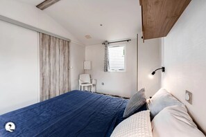 Quarto com cama, uma cadeira, uma janela e um vigamento de madeira no teto.