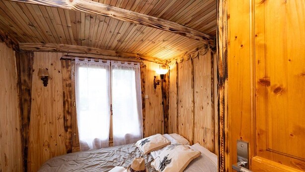 Ein Zimmer aus Holz mit einem Bett, einer Tür und einem Fenster mit Vorhängen.