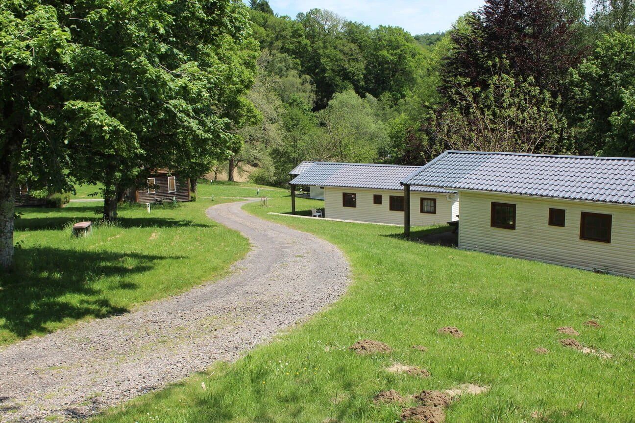 A gravel path leading to a row of cabins with a grassy field and trees in the background.