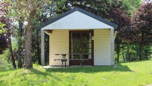 A small, single-story building with a gabled roof, a wooden bench outside, and a sign that reads "CLOTHES".