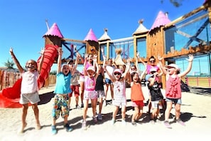 A group of children playing on a playground with slides and climbing structures.