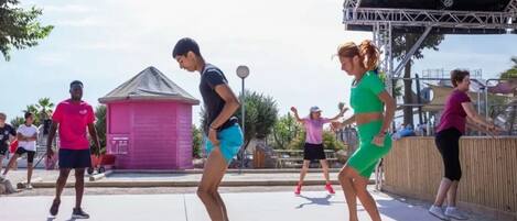 A group of people exercising outdoors with a stage and a small building in the background.