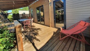 Eine Holzterrasse mit Tisch und Stühlen, ein rotes Liegestuhl und ein überdachter Bereich mit einer Pergola.