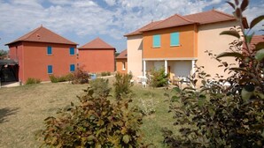 Un edificio residencial con techo rojo, fachada color beige y un pequeño jardín con césped y arbustos.