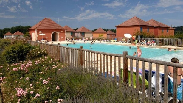Un área de piscina con varias piscinas, rodeada de edificios con tejados rojos y una cerca de madera.