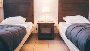 Una habitación con dos camas, una mesita de noche con lámpara y suelo de baldosas.