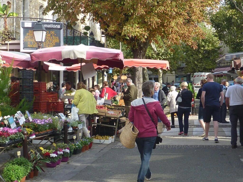 A street market with vendors and customers, outdoor seating, and a sign for 'mations.'
