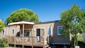 Enjoy the serene surroundings from the covered patio area of this mobile home, which features multiple windows and a door.