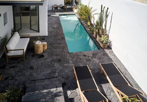 A modern outdoor pool area with stone flooring, lounge chairs, and potted plants. - Arithera Villa in Santorini (Santorini)